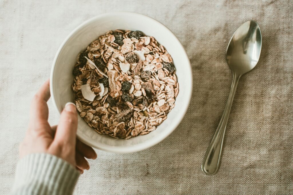 A close-up of a healthy muesli breakfast bowl with a hand and spoon on a table.